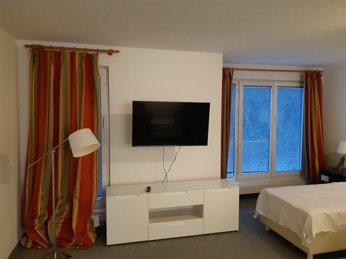 Wohnbereich mit Fernseher an der Wand und weißem Lowboard neben dem Bett